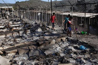 epa08656942 Asylum seekers walk among debris in the Moria refugees camp on the island of Lesbos, Greece, 09 September 2020. According to reports, a fire broke out at Moria Camp early on 09 September, after approximately 35 refugees, who had tested positive for COVID-19, refused to move into isolation with their families.  EPA/ORESTIS PANAGIOTOU
