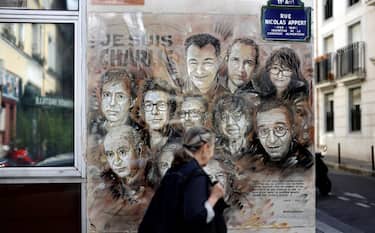 TOPSHOT - A woman walks past a painting by French street artist and painter Christian Guemy, known as C215, in tribute to members of Charlie Hebdo newspaper who were killed by jihadist gunmen in January 2015, in Paris, on August 31, 2020. - Fourteen alleged accomplices in the 2015 jihadist attacks on the Charlie Hebdo satirical weekly, on a kosher supermarket and in the southern Paris suburb Montrouge go on trial on September 2, more than half-a-decade after days of bloodshed that still shock France. The attacks heralded a wave of Islamist violence that has left 258 people dead and raised unsettling questions about modern France's ability to preserve security and harmony for a multicultural society. (Photo by THOMAS COEX / AFP) / RESTRICTED TO EDITORIAL USE - MANDATORY MENTION OF THE ARTIST UPON PUBLICATION - TO ILLUSTRATE THE EVENT AS SPECIFIED IN THE CAPTION (Photo by THOMAS COEX/AFP via Getty Images)