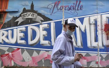 A man wearing a face mask  walks in front of a graffito  in Marseille, southeastern France, on September 14, 2020, amid the Covid-19 pandemic, caused by the novel coronavirus. (Photo by NICOLAS TUCAT / AFP) (Photo by NICOLAS TUCAT/AFP via Getty Images)
