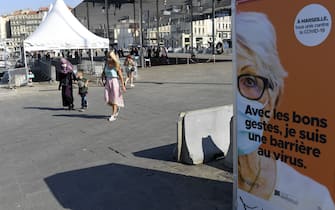 Pedestrians wearing face masks walk near a sign reading "With the good gestures, I am a barrier to the virus" on the Vieux-Port of Marseille, southeastern France, on September 14, 2020, amid the Covid-19 pandemic, caused by the novel coronavirus. (Photo by NICOLAS TUCAT / AFP) (Photo by NICOLAS TUCAT/AFP via Getty Images)