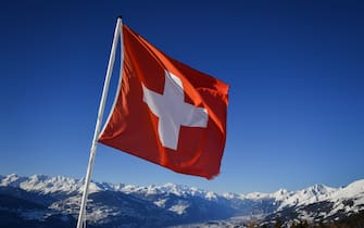 A Swiss flag flutters on March 4, 2018 in Crans-Montana above the Rhone valley in the Swiss canton of Valais, location of Sion, a city of some 34,000 souls bidding to host the 2026 Winter Olympic Games. - The official race to succeed 2018 hosts Pyeongchang, and Beijing in 2022 begins in March when would be candidates file "letters of intention" to the International Olympic Committee. (Photo by Fabrice COFFRINI / AFP) (Photo by FABRICE COFFRINI/AFP via Getty Images)