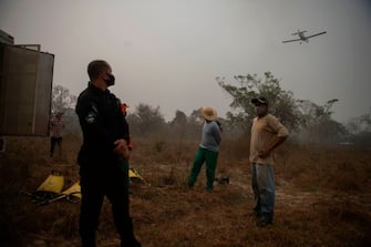 Inmates and correctional officers look at a plane flying over them to throw water on fires at the wetlands of the Pantanal, near Transpantaneira park road in Mato Grosso state, Brazil, on September 17, 2020. - The Pantanal, the world's biggest tropical wetlands, is being devastated by record wildfires which are destroying vast areas of vegetation and threatening wildlife. (Photo by MAURO PIMENTEL / AFP) (Photo by MAURO PIMENTEL/AFP via Getty Images)