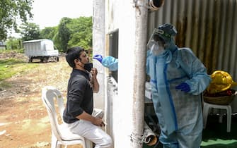 TOPSHOT - A health worker (R) wearing personal protective equipment (PPE) collects a swab sample from a resident for a Covid-19 coronavirus test at a temporarory collection centre in Secunderabad, the twin city of Hyderabad on October 1, 2020. (Photo by NOAH SEELAM / AFP) (Photo by NOAH SEELAM/AFP via Getty Images)