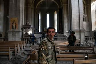A man with a military outfit stands as journalists report on October 8, 2020 inside the damaged Ghazanchetsots (Holy Saviour) Cathedral in the historic city of Shusha, some 15 kilometers from the disputed Nagorno-Karabakh province's capital Stepanakert, that was hit by a bomb as fighting between Armenian and Azerbaijani forces spilled over today ahead of a first meeting of international mediators in Geneva. - Nagorno-Karabakh broke away from Azerbaijan in a 1990s war that claimed the lives of some 30,000 people. The Armenian separatists declared independence, but no countries recognise its autonomy and it is still acknowledged by world leaders as part of Azerbaijan. (Photo by ARIS MESSINIS / AFP) (Photo by ARIS MESSINIS/AFP via Getty Images)