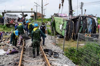 Investigators work by the wreckage of an overturned bus involved in a deadly collision with a train at Khlong Kwaeng Klan railway station in Chachoengsao province, east of the Thai capital Bangkok, on October 11, 2020. (Photo by Mladen ANTONOV / AFP) (Photo by MLADEN ANTONOV/AFP via Getty Images)