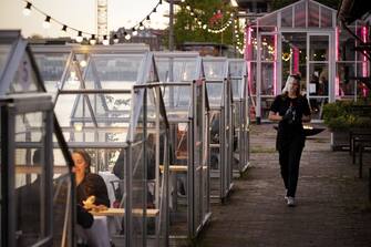 A waitres wearing a protective faceshield arrives to serve wine to friends having dinner in a so-called quarantine greenhouses in Amsterdam, on May 5, 2020 as the country fights against the spread of the COVID-19, the novel coronavirus. (Photo by Robin VAN LONKHUIJSEN / ANP / AFP) / Netherlands OUT (Photo by ROBIN VAN LONKHUIJSEN/ANP/AFP via Getty Images)