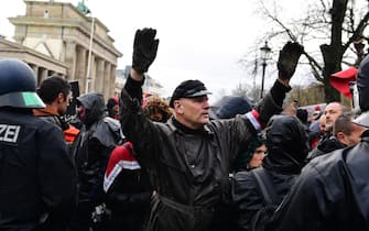 epa08827170 A man wearing an armlet with the colors of the flag of the former German Empire raises his arms during a demonstration against German coronavirus restrictions, near the Brandenburg Gate in Berlin, Germany, 18 November 2020. While German interior minister prohibited demonstrations around the Reichstag building during the parliamentary Bundestag session people gathered to protest against government-imposed semi-lockdown measures aimed at curbing the spread of the coronavirus pandemic. Since 02 November, all restaurants, bars, cultural venues, fitness studious, cinemas and sports halls are forced to close for four weeks as a lockdown measure to rein in skyrocketing coronavirus infection rates.  EPA/FILIP SINGER