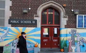 epa08828423 A person walks past a public school in Brooklyn, New York, USA, 18 November 2020. New York City Mayor Bill de Blasio announced on 18 November that the city s entire public school system, the largest in the country, will indefinitely suspend all in-school classes as a result of the rising COVID-19 positivity rate from 19 november 2020..  EPA/JUSTIN LANE