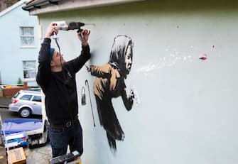 BRITAIN ARTS BANKSY epa08875161 Fred Loosmore places a protective perspex covering over the new creation entitled 'Aachoo!!' by British street artist Banksy that appeared on Vale Street overnight in Bristol, Britain, 10 December 2020. The painting depicts an old woman sneezing with her false teeth flying out. EPA/JON ROWLEY