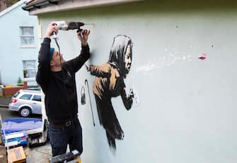 epa08875161 Fred Loosmore places a protective perspex covering over the new creation entitled 'Aachoo!!' by British street artist Banksy that appeared on Vale Street overnight in Bristol, Britain, 10 December 2020. The painting depicts an old woman sneezing with her false teeth flying out.  EPA/JON ROWLEY