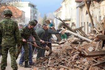 Croatian soldiers and people clean rubble next to damaged buildings in Petrinja, some 50kms from Zagreb, after the town was hit by an earthquake of the magnitude of 6,4 on December 29, 2020. - The tremor, one of the strongest to rock Croatia in recent years, collapsed rooftops in Petrinja, home to some 20,000 people, and left the streets strewn with bricks and other debris. Rescue workers and the army were deployed to search for trapped residents, as a girl was reported dead. (Photo by Damir SENCAR / AFP)