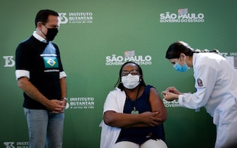 epa08944696 Monica Calazans (C), a nurse at Hospital las Clinicas in the capital of Sao Paulo, receives the vaccine against covid-19 in the presence of the governor of the state of Sao Paulo, Joao Doria (L), in Sao Paulo, Brazil, 17 January 2021. Brazil, one of the countries in the world most affected by the coronavirus pandemic, applied the first dose of the covid-19 vaccine to the 54-year-old nurse this Sunday in Sao Paulo, at a time when the Latin American giant faces a second wave of the disease. The first dose of the vaccine developed by the Chinese laboratory Sinovac and the Brazilian Butantan Institute was administered just minutes after the approval of its emergency use by the National Health Surveillance Agency (Anvisa).  EPA/Fernando Bizerra Jr