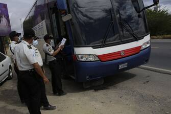 1297091566 RIO HONDO, GUATEMALA - JANUARY 18: Police officers check a bus at a registration booth on January 18, 2021 in Rio Hondo, Zacapa, Guatemala. The caravan departed from Honduras to walk across Guatemala and Mexico to eventually reach the United States. After clashing with the police yesterday migrants are being held to carry out immigration and heath controls. Central Americans expect to receive asylum and most Hondurans decided to migrate after being hit by recent hurricanes. (Photo by Josue Decavele/Getty Images)