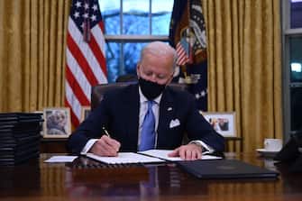 TOPSHOT - US President Joe Biden sits in the Oval Office as he signs a series of orders at the White House in Washington, DC, after being sworn in at the US Capitol on January 20, 2021. - US President Joe Biden signed a raft of executive orders to launch his administration, including a decision to rejoin the Paris climate accord. The orders were aimed at reversing decisions by his predecessor, reversing the process of leaving the World Health Organization, ending the ban on entries from mostly Muslim-majority countries, bolstering environmental protections and strengthening the fight against Covid-19. (Photo by Jim WATSON / AFP)