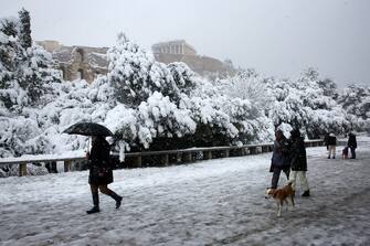 epa09015829 People walk under the hill of Acropolis during heavy snowfall, in Athens, Greece, 16 February 2021. As the cold front Medea sweeping over Greece was in full progress and heading south, very low temperatures were recorded in the northern parts of the country.  EPA/ORESTIS PANAGIOTOU