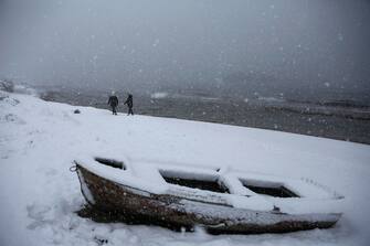 epa09016289 Two women walk behind a boat at a snowy beach during heavy snowfall in the coastal suburb of Lagonissi, near Athens, Greece, 16 February 2021. As the cold front 'Medea' is sweeping over Greece in full progress and heading south, very low temperatures were recorded in the northern parts of the country.  EPA/YANNIS KOLESIDIS