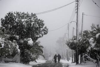 epa09016290 Two men walk during heavy snowfall in the suburb of Kalyvia, south of Athens, Greece, 16 February 2021. As the cold front 'Medea' is sweeping over Greece in full progress and heading south, very low temperatures were recorded in the northern parts of the country.  EPA/YANNIS KOLESIDIS