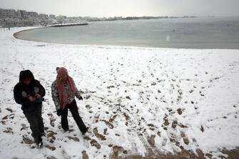 epa09015968 A couple walks on the snowy beach of Alimos, as the heavy snowfall continues in the southern suburbs of Athens, Greece, 16 February 2021. The severe bad weather continues with intense phenomena and heavy snowfall that have closed many roads and have created intense problems in transportation.  EPA/ALEXANDER BELTES
