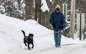 epa09017044 A man walks a dog on a snowy street after an overnight snowfall left more than 18 inches (45.72cm) on the ground and roadways in Winnetka, Illinois, USA, 16 February 2021. Much of the US has been in the grip of winter storms that have sent temperatures plummeting, closed major airports, and caused power outages to millions of people.  EPA/TANNEN MAURY