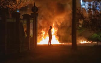 A boy stands and looks on as flames and smoke rises behind him at the scene of violence in Newtownabbey, north of Belfast, in Northern Ireland on April 3, 2021. - The disturbance in the Loyalist area north of Belfast, where petrol bombs were thrown and cars were set alight, follows a night of violence in the Northern Ireland capital in which police officers were injured prompting calls for calm. It is thought rising discontent among unionist pro-British factions in Northern Ireland over arrangements aimed at preserving a fragile peace in the territory by preventing a hard border with EU member Ireland is fueling anger. Tension has also been stoked this week by a decision not to prosecute 24 Sinn Fein party members who attended the funeral in June of Irish Republican Army figure Bobby Storey in blatant violation of of Covid-19 guidelines. (Photo by PAUL FAITH / AFP) (Photo by PAUL FAITH/AFP via Getty Images)