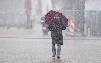 05 April 2021, Berlin: A man walks with an umbrella in a snowstorm on Pariser Platz in front of the Brandenburg Gate. Photo: Christophe Gateau/dpa (Photo by Christophe Gateau/picture alliance via Getty Images)