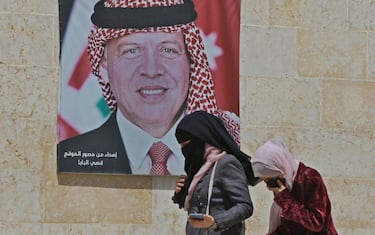 Women walk past a poster of Jordan's King Abdullah II on a street in the capital Amman, on April 6, 2021, after a security crackdown revealed tensions in the monarchy. (Photo by Khalil MAZRAAWI / AFP) (Photo by KHALIL MAZRAAWI/AFP via Getty Images)