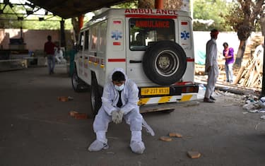 epa09167847 A worker in personal Protective Equipment (PPE) rests near an ambulance at a cremation ground in New Delhi, India, 29 April 2021. Delhi reported 25,986 fresh cases, 368 deaths in last 24 hours and continue to struggle with the oxygen supply. EPA/IDREES MOHAMMED