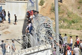 epa09210803 Migrants climb the fence in the northern town of Fnideq in an attempt to cross the border from Morocco to the Spanish enclave of Ceuta, in North Africa 18 May 2021.  In little over 24 hours a total of almost 8,000 people entered into the Spanish city of Ceuta, located in the North African coast, by sea side and hundreds of migrants continue to attempt doing so. The Spanish authorities have deployed the army to patrol on the border separating Ceuta in the Spanish side from the Moroccan side, in a bid to control this latest surge of entry attempts.  EPA/JALAL MORCHIDI