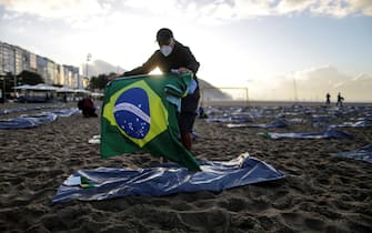 Un membro dell'ONG di Rio de la Paz con una bandiera brasiliana durante i preparativi per una cerimonia in memoria delle vittime del Covid-19 sulla spiaggia di Copacabana a Rio de Janeiro, Brasile
