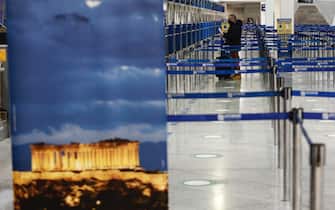 Un passeggero nel terminal delle partenze accanto a un poster raffigurante il tempio del Partenone, all'aeroporto internazionale Eleftherios Venizelos di Atene