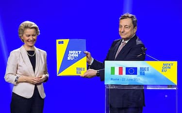 Italy's Prime Minister, Mario Draghi holds the NextGenerationEU recovery plan after it was handed to him by European Commission President, Ursula von der Leyen (L) during a joint press conference on June 22, 2021 at Rome's Cinecitta cinema studio, following their meeting as part of Leyen's tour of Europe to launch Covid-19 recovery plans. (Photo by Alberto PIZZOLI / AFP) (Photo by ALBERTO PIZZOLI/AFP via Getty Images)