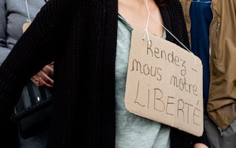 A demonstrator has a sign reading "Give us back our freedom" hanging around her neck, as on July 14, 2021, 2 days after the last speech of the President of the French Republic Emmanuel Macron to introduce mandatory vaccination of caregivers and the generalization of the Health Pass in public places of more than 50 people to cope with a resurgence of Covid in France following the emergence of the Delta variant, several hundred people gathered in the streets of Paris to demonstrate their opposition.  This demonstration was quickly repressed by the riot police creating clashes with the demonstrators, many of whom claimed to be Yellow Vests. (Photo by Samuel Boivin/NurPhoto)