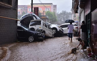 DENGFENG, CHINA - JULY 20: People look at damaged vehicles in a flooded street on July 20, 2021 in Dengfeng, Zhengzhou City, Henan Province of China. Torrential rains hit Henan since July 16, causing floods in many parts of the province on Monday and Tuesday. (Photo by VCG/VCG via Getty Images)