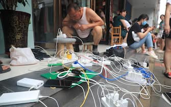 ZHENGZHOU, CHINA - JULY 22: People charge their mobile phones outside a shop on July 22, 2021 in Zhengzhou, Henan Province of China. Torrential rains across Henan Province cut off power supply in Zhengzhou and some shops provide extension power sockets for citizens for free. (Photo by Wang Fuxiao/VCG via Getty Images)