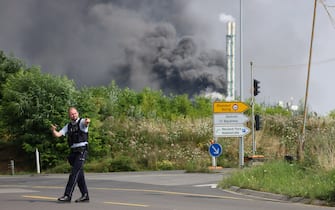27 July 2021, North Rhine-Westphalia, Leverkusen: A policeman is standing near an access road to the Chempark over which a dark cloud of smoke is rising. After an explosion fire brigade, rescue forces and police are currently in large-scale operation, the police explained. Due to the damage, the busy A1 motorway near Leverkusen has been closed. Photo: Oliver Berg/dpa (Photo by Oliver Berg/picture alliance via Getty Images)