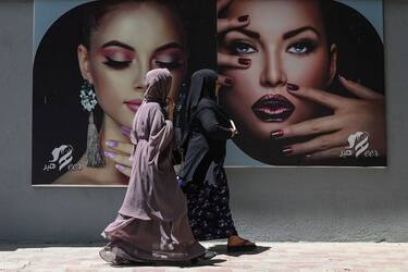 Burqa clad women walk past a billboard put up on the wall of a beauty salon in Kabul on August 7, 2021. (Photo by SAJJAD HUSSAIN / AFP) (Photo by SAJJAD HUSSAIN/AFP via Getty Images)