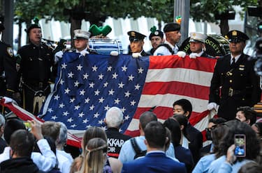 Members of the Fire Department of New York (FDNY) and New York City Police Department (NYPD) carry a damaged American flag near the memorial pools at the National September 11 Memorial & Museum during a commemoration ceremony for the 20th anniversary of the 9/11 attacks in New York, U.S, on Saturday, Sept. 11, 2021. The milestone comes just after the U.S disengaged from its longest war, in Afghanistan, where the attacks were planed. Photographer: Jonathan Alpeyrie/Bloomberg via Getty Images