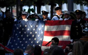 epa09460981 New York police and firefighters hold a US flag as a band plays the US National Anthem at the National 9/11 Memorial during a ceremony commemorating  the 20th anniversary of the 9/11 attacks on the World Trade Center, in New York, on September 11, 2021.  EPA/ED JONES / POOL