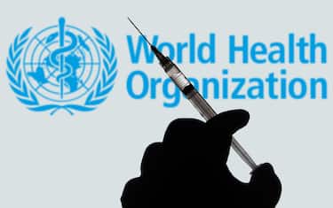 BRAZIL - 2021/04/02: In this photo illustration, a hand holds a medical syringe with a World Health Organization (WHO) company logo displayed on a screen in the background. (Photo Illustration by Rafael Henrique/SOPA Images/LightRocket via Getty Images)
