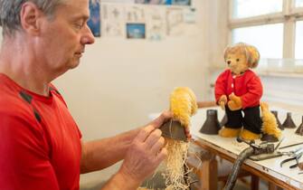 PRODUCTION - 16 September 2021, Bavaria, Coburg: Wooden wool stopper Uwe Olunczek works on a Merkel teddy. The Hermann teddy factory in Coburg has stuffed bears in its range that are reminiscent of King Ludwig, B. Obama or the Queen of the United Kingdom - now Angela Merkel has also been added. With its wig, clothes, "Germany chain" and "Merkel rhombus", the teddy bear is reminiscent of the German Chancellor. Photo: Nicolas Armer/dpa (Photo by Nicolas Armer/picture alliance via Getty Images)
