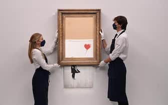 Gallery employees pose for photographers next to a painting entitled 'Love is in the Bin' by anonymous British street artist Banksy at Sotheby's auction house in London, Britain 03 September 2021. ANSA/FACUNDO ARRIZABALAGA