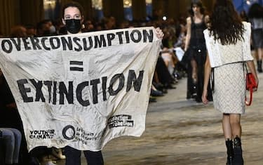 A demonstrator holds a banner as models present creations by Louis Vuitton during the Women's Spring-Summer 2022 Ready-to-Wear collection fashion show as part of Paris Fashion Week at the Louvre in Paris, on October 5, 2021. - Extinction Rebellion activists burst into the Louis Vuitton fashion show at the Louvre to denounce the impact of the fashion industry on climate change, on the last day of Paris Fashion Week. (Photo by Christophe ARCHAMBAULT / AFP) (Photo by CHRISTOPHE ARCHAMBAULT/AFP via Getty Images)