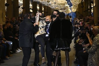 A demonstrator is being evicted by security members as models present a creation by Louis Vuitton during the Women's Spring-Summer 2022 Ready-to-Wear collection fashion show as part of Paris Fashion Week at the Louvre in Paris, on October 5, 2021. - Extinction Rebellion activists burst into the Louis Vuitton fashion show at the Louvre to denounce the impact of the fashion industry on climate change, on the last day of Paris Fashion Week. (Photo by Christophe ARCHAMBAULT / AFP) (Photo by CHRISTOPHE ARCHAMBAULT/AFP via Getty Images)