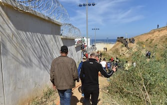 epa09209372 Migrants walk along a border wall in the northern town of Fnideq in an attempt to cross the border from Morocco to the Spanish enclave of Ceuta, in North Africa, 18 May 2021.  At least 5,000 migrants, an unprecedented influx in Spanish authorities said a period of high tension between Madrid and Rabat crept into Ceuta on 17 May, a record for a day. They reached the coast by swimming or walking at low tide from beaches a few kilometers to the south, some using inflatable swimming rings.  EPA/JALAL MORCHIDI