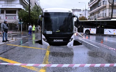 epa09524704 A view of a passenger bus after it fell with the front part into a five-meter pit while carrying 15 passengers, in a central avenue in Thessaloniki, northern Greece, 15 October 2021, as heavy rainfall hit the city. No injuries have been reported and the passengers were safely evacuated.  EPA/DIMITRIS TOSIDIS