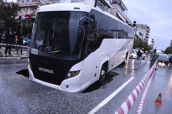 epa09524701 A view of a passenger bus after it fell with the front part into a five-meter pit while carrying 15 passengers, in a central avenue in Thessaloniki, northern Greece, 15 October 2021, as heavy rainfall hit the city. No injuries have been reported and the passengers were safely evacuated.  EPA/DIMITRIS TOSIDIS