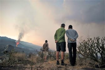 People observe as the Cumbre Vieja volcano spews lava, ash and smoke, in Los Llanos de Aridane, in the Canary Island of La Palma on October 10, 2021. - It has been almost three weeks since La Cumbre Vieja began erupting, forcing 6,000 people from their homes as the lava scorched its way across 1,200 acres of land. Earlier on October 9, part of the volcano's cone collapsed, sending new rivers of lava pouring down the slopes towards an industrial zone. (Photo by JORGE GUERRERO / AFP) (Photo by JORGE GUERRERO/AFP via Getty Images)
