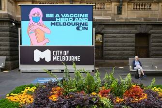1236017757 A woman sits outside a vaccination centre in Melbourne on October 21, 2021, ahead of the expected lifting of coronavirus restrictions in one of the world's most locked-down cities at midnight. (Photo by William WEST / AFP) (Photo by WILLIAM WEST/AFP via Getty Images)