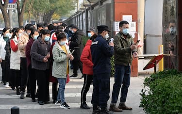 People wait in line to receive Covid-19 coronavirus vaccination booster shots as a security guard checks body temperature of a man along a street in Beijing on October 30, 2021. (Photo by Jade GAO / AFP) (Photo by JADE GAO/AFP via Getty Images)