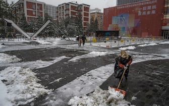 BEIJING, CHINA - NOVEMBER 07: A worker shovels snow from in front of a shopping mall following a snowfall on November 7, 2021 in Beijing, China.  Beijing, which averages less than seven days of snow annually, is set to host the Beijing 2022 Winter Olympics next February. (Photo by Kevin Frayer/Getty Images)